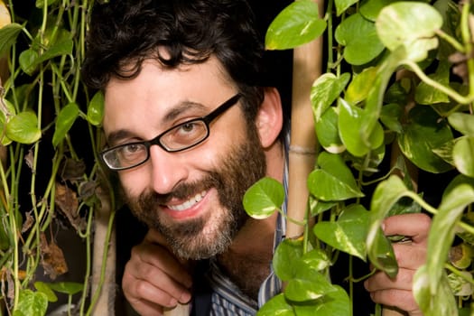 Portrait of a mature man peeking through plants and smiling