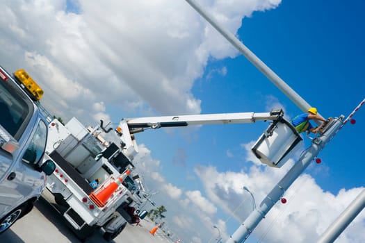 Low angle view of a maintenance engineer on a mobile crane repairing a security camera on a pole