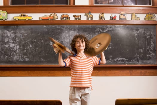 Schoolboy playing cymbals in front of a blackboard