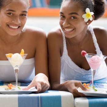 Two female friends holding ice creams at poolside
