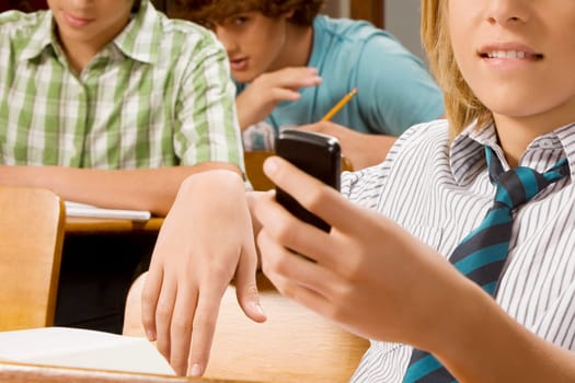 Teenage boy text messaging on a mobile phone in a classroom