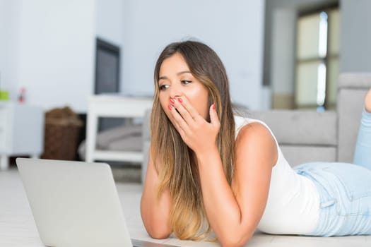 Beautiful young woman relaxing at home on her laptop computer