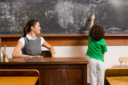 Schoolboy pointing at a blackboard with a teacher in a classroom