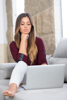 Beautiful young woman relaxing at home on her laptop computer