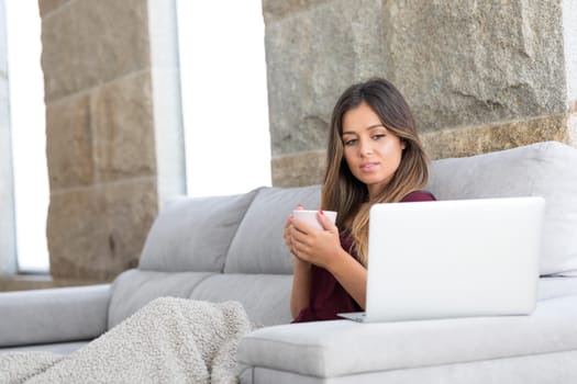 Beautiful young woman relaxing at home on her laptop computer