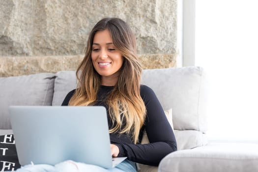 Beautiful young woman relaxing at home on her laptop computer