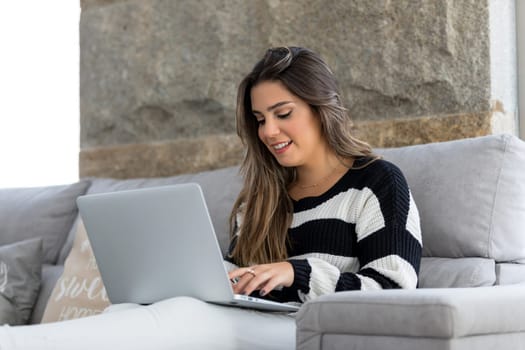 Beautiful young woman relaxing at home on her laptop computer
