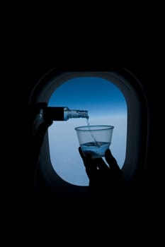 Person pouring whiskey into a glass in front of an airplane window