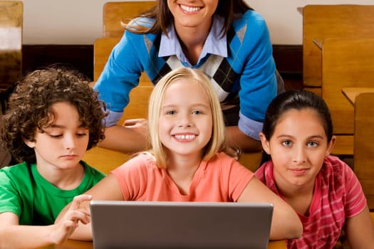 Students with their teacher using a laptop in a classroom