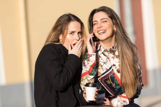 Young pretty girls best friends smiling and having fun, walking at the city. Shopping. Wearing stylish outerwear. Bright make up. Positive emotions. Outdoors lifestyle fashion close up portrait