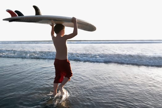 Boy carrying a surfboard on the beach
