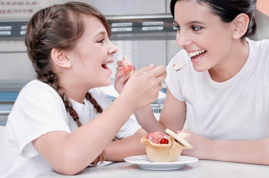 Girl and a teenage girl feeding ice cream to each other
