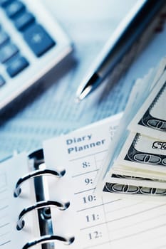 Close_up of a spiral notebook and US paper currency with a calculator