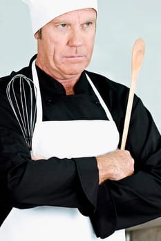 Chef holding a wooden spoon and a wire whisk