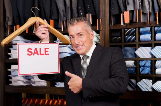 Businessman holding a Sale sign in a clothing store