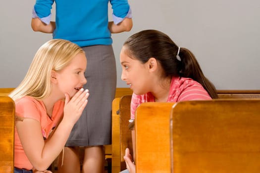 Schoolgirl whispering to her friend in a classroom