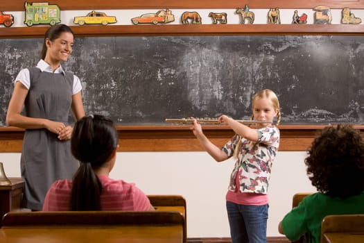 Schoolgirl playing a flute with her teacher and classmates in a classroom