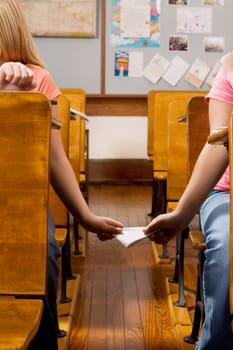 Two schoolgirls passing note during exam in a classroom