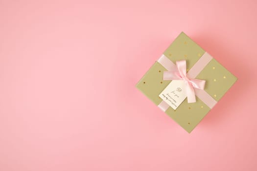 Golden box with ribbon lying on pink background with copy space. Wrapped gift on table with space for text. Valentine s present in flat lay composition.