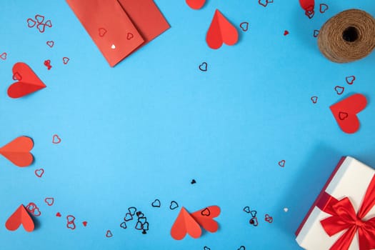 Blue background with gift, envelope and papper hearts. Present with love symbols on the sides with copy space in center. Valentine theme from above in flat lay composition.