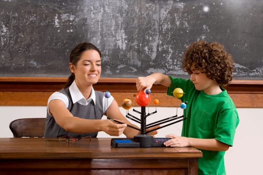 Schoolboy and his teacher with model of solar system in a classroom