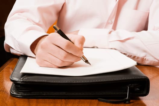 Mid section view of a businessman writing on a sheet of paper with a pen