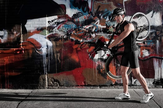 Man carrying a bicycle on his shoulders in front of a graffiti covered wall
