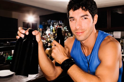 Close_up of a young man sitting at a bar counter and holding beer bottles