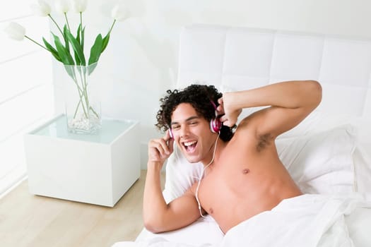 High angle view of a young man lying on the bed and listening to music