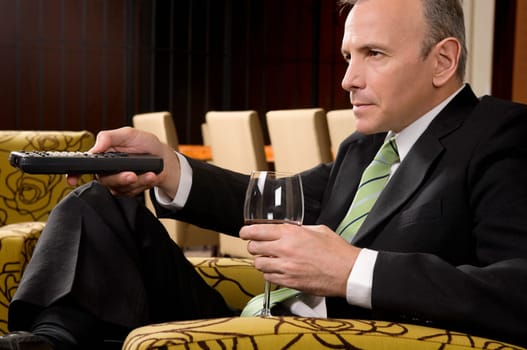 Businessman operating a remote control and holding a wine glass