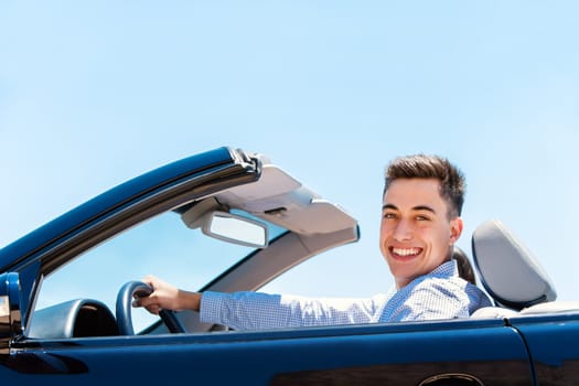 Portrait of handsome young smiling man driving luxurious blue convertible.