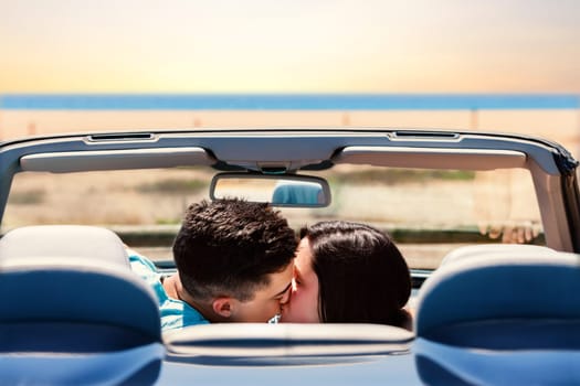 Portrait of young couple kissing in convertible. Rear view of couple in car next to beach.