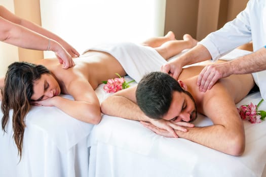 Close up of young couple enjoying simultaneous body massage in spa. Two therapists doing back massage on couple at the same time.