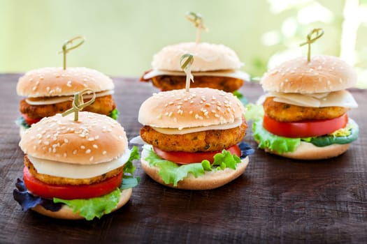 Macro close up of multiple mini chicken burgers on wooden surface.