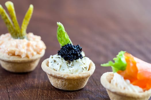 Macro close up Mini savory tartlets on wooden surface.Focus point of tartlet filled with cottage cheese and black cod caviar..