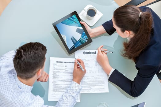 Young business couple discussing rental agreement. Woman showing man office buildings on digital tablet at table.