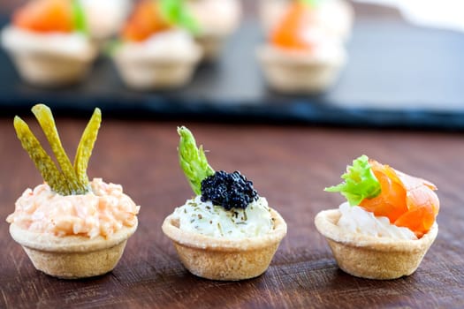 Macro close up of three Mini puff open pastry tartlets topped with different seafood fillings. Tartlet platter out of focus in background with copy space..