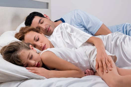 Mid adult couple sleeping with their daughter