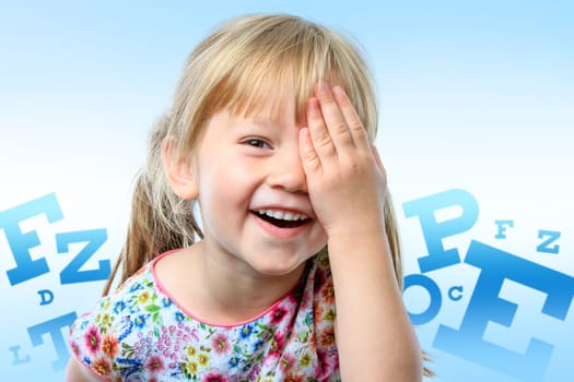 Close up fun portrait of little girl closing on eye with hand.Big block letter conceptual eye chart in background.