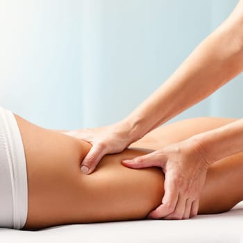 Macro close up of Osteopathic hamstring massage.Therapist applying pressure with hands on back go female leg.