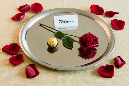 Close_up of a rose with sweet food and welcome note in a plate