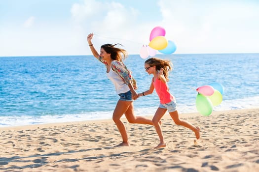 Action portrait of Young girls running with colorful balloons on beach.