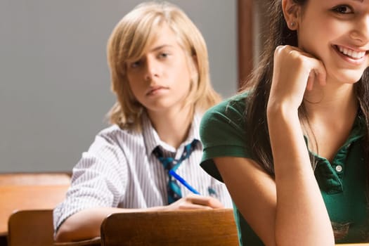 Teenage girl smiling with her classmate sitting behind him