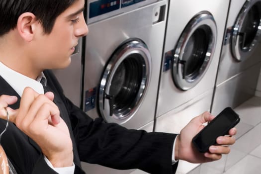 Businessman text messaging on a mobile phone in a laundromat