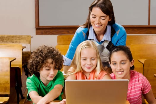 Students with their teacher using a laptop in a classroom