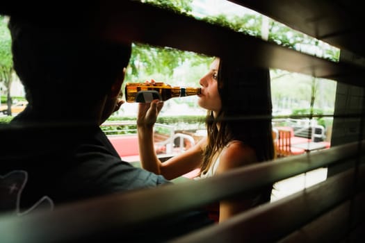 Side profile of a young woman drinking beer with a young man sitting beside her