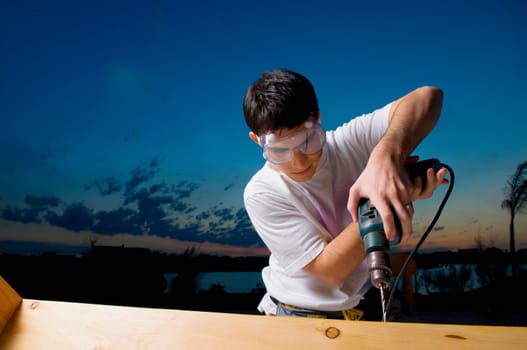 Young man drilling a wooden plank