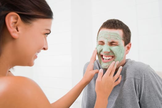 Young woman touching the facial mask of a young man and smiling