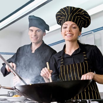 Female and a male chef cooking food in the kitchen
