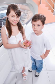Girl holding a glass of ice cream and standing with her brother